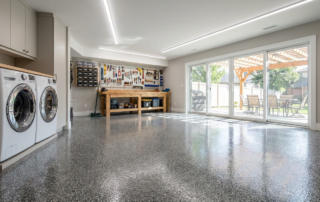 Gray flake basement floor epoxy coating in a finished workshop, with a laundry area and covered patio doors beyond